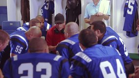 Football players have a meeting in the locker, listen to a speech from the coach, and get ready for the game