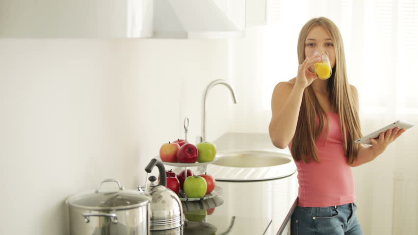 Beautiful girl in kitchen drinking juice using touchpad and smiling