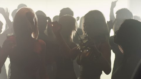 A group of attractive silhouetted young adults dance in a smokey club in slow motion