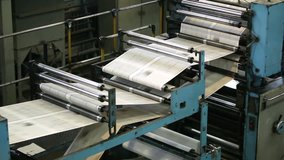 Black-and-white newspaper sheets moving through rollers along the production line