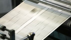 Close-up of an uncut sheet of a black-and-white newspaper going through numerous rollers and cylinders