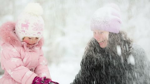 Happy woman and child playing with snow in winter park. Slow motion