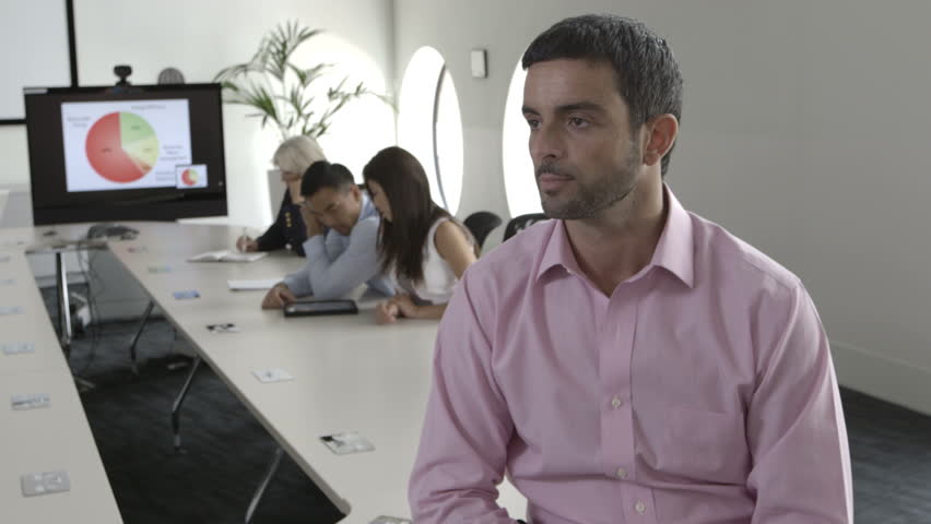 MS Man sitting with arms crossed while people working in background