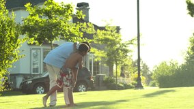 A father plays with his son in the grass on the lawn by picking up and swinging him around
