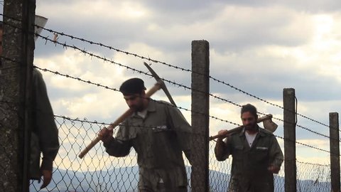 Prisoners passing behind a barbed wire through the shot, close up.