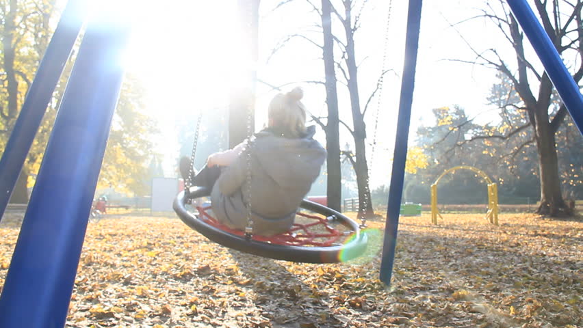 Mother and child play on swing at the playground in autumn with flare