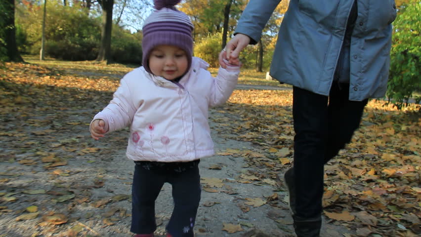 Baby hold her moms hand and learns to walk in a park