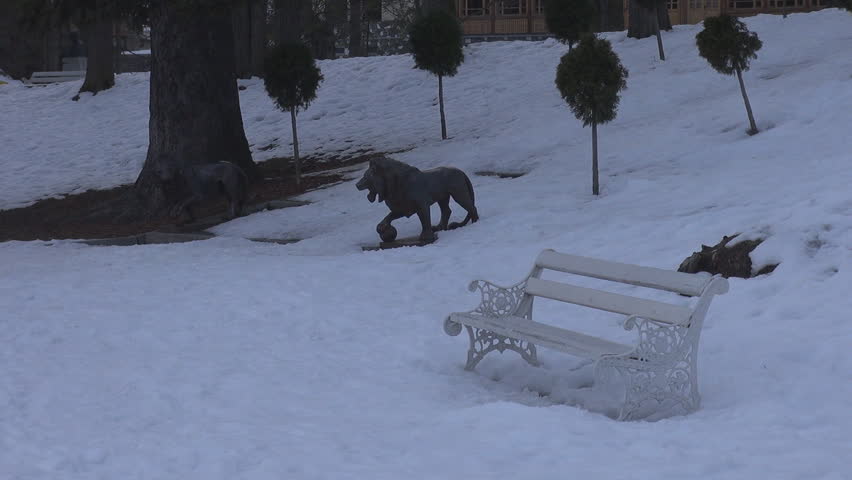 Empty bench in city park covered by snow in cloudy day, winter time