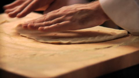 Close up of a chef preparing a pizza pie from scratch in his kitchen with a brick oven