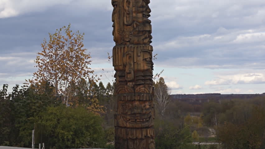 Wooden Oroqen totem pole on the cloudy sky background, pan up. Northeast China, Heilongjiang Province, near the city of Heihe.