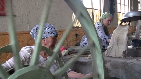 MARGILON, UZBEKISTAN - 10 JUNE 2013: Two women are busy steaming and unravelling silk cocoons in Margilon, Uzbekistan