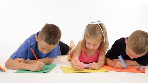 Three children lying on the floor coloring on bright colored paper. Dolly footage.