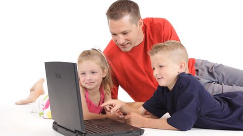 A dad on the floor with his little girl and young son, looking at something on the laptop. Dolly footage.