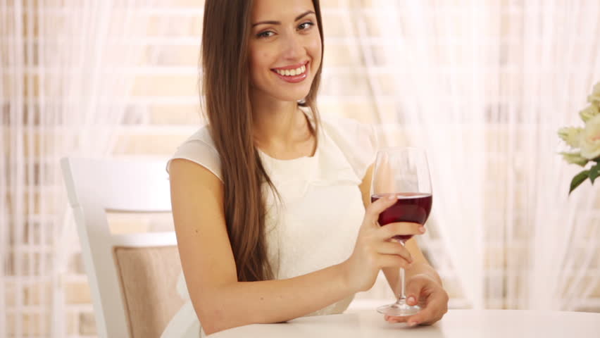 Pretty young woman sitting at cafe with glass of wine looking at camera and