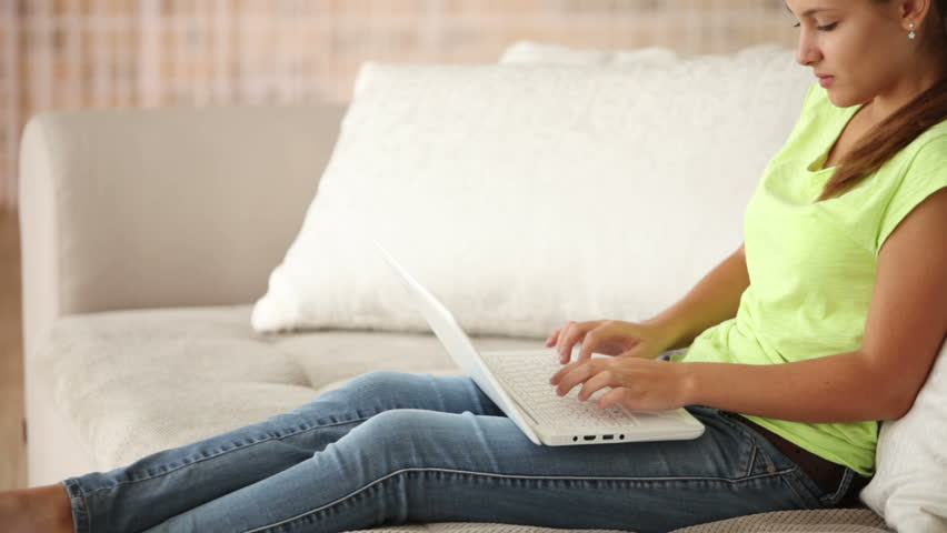 Cheerful girl sitting on sofa with laptop holding credit card looking at camera