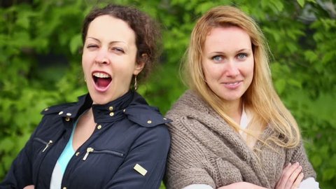 Two young woman look and yawn against green foliage