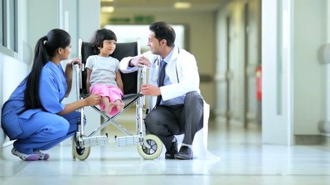Male pediatrician and female nurse explain medical treatment to young patient in wheelchair in hallway