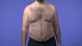 Hairy overweight man lifting weights. High definition video shot on studio blue screen.
