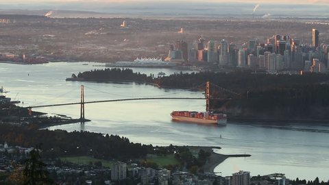 A high angle view of downtown Vancouver, the Lions Gate Bridge, and Burrard Inlet at sunrise. A freighter passes under the bridge as the sun comes up. British Columbia, Canada.