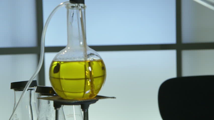 Panning down from substance boiling in laboratory flask to a gun and other paraphernalia of sinister looking scene.
