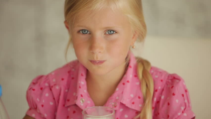 Charming little girl drinking milk and smiling at camera