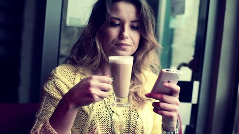 Woman with smartphone drinking cafe latte in cafe
