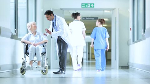 Hallway view in busy modern medical facility with medical professionals and doctor chatting with wheelchair-bound patient
