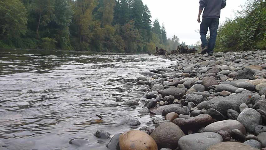 Model released man walking along river as boat drives by in Oregon wilderness.