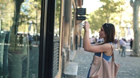Woman taking photo of clothes on shop window in the city
