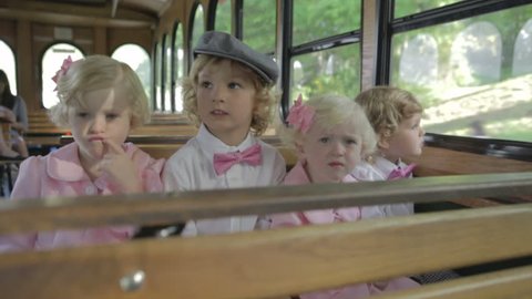 Young children all dressed up sitting on trolley seat together. Happy boys and girls together dressed in pink.