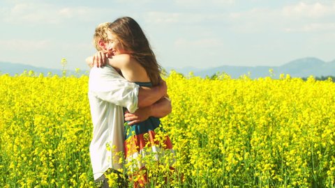 A young attractive couple dance and hug in a wide open yellow field on a sunny day