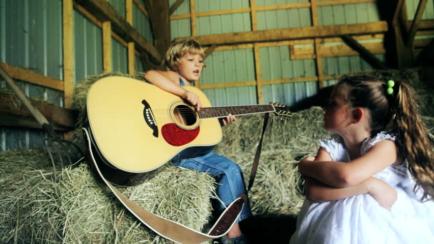 Child playing and singing with guitar in the barn. Children starting a country band together in the barn on the farm. Country music being sung by children.