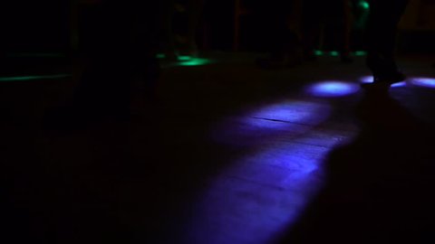 people dance at a party, perspective to ground and few pairs of feet within the strobe light