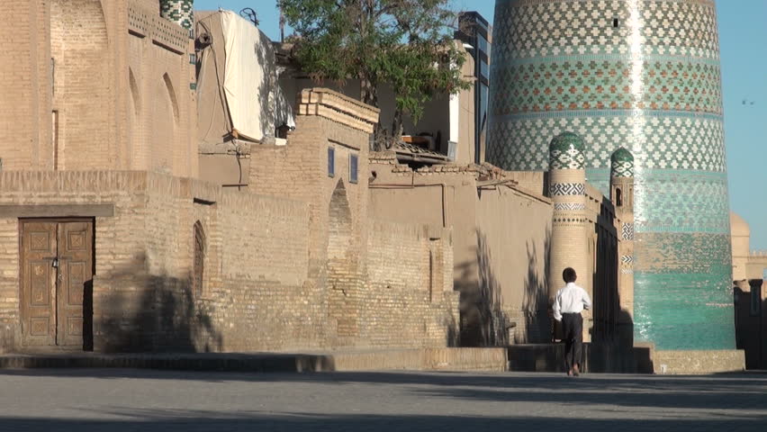 KHIVA, UZBEKISTAN - 27 MAY 2013: A schoolboy walks towards school, passing a beautifully colored minaret, inside the walled city of Khiva, Uzbekistan