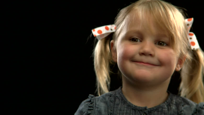 A cute young blonde girl with pigtails looks away shyly on a black background