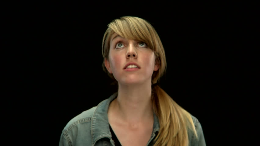 A cute young white woman looks up in the air on a black background