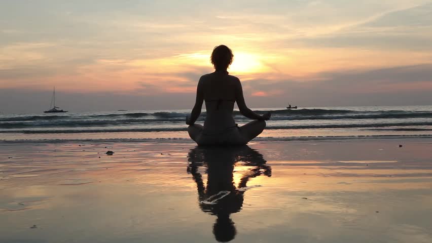 Silhouette young woman practicing yoga on the beach at sunset.(HD)