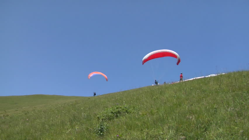 Paraglider launching from the ridge with an colorful canopy against a blue sky.