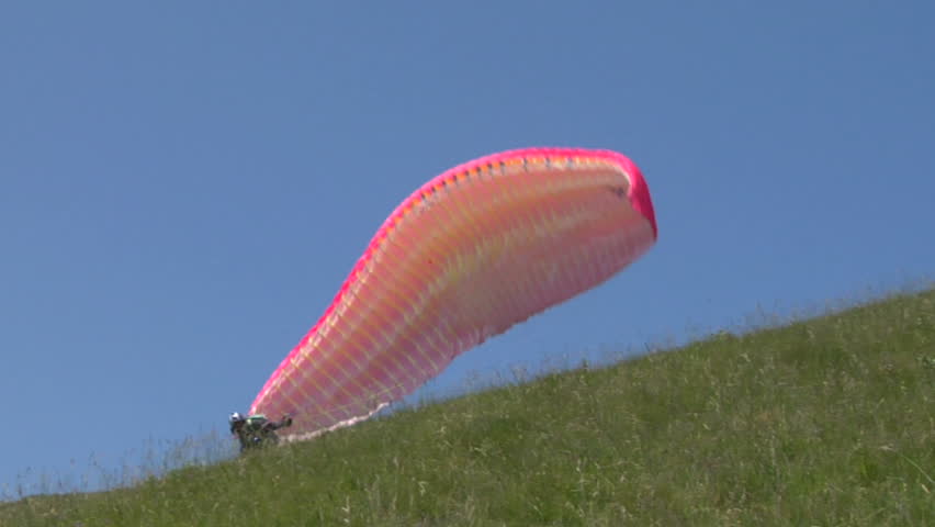 Paraglider launching from the ridge with an colorful canopy against a blue sky.