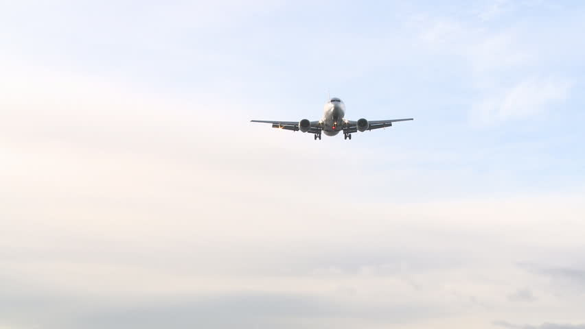 A wide view of a large jet plane coming in over the sea to land on a runway