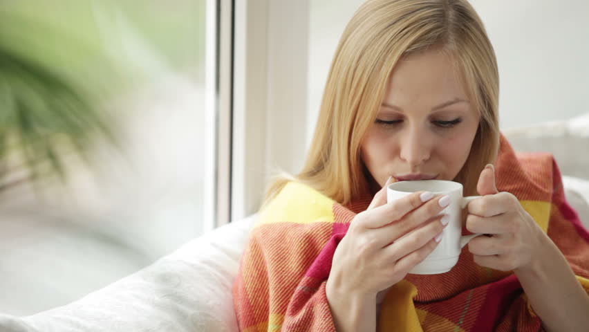 Charming young woman relaxing on sofa holding cup of tea looking at camera and