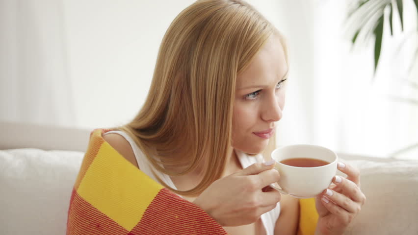 Beautiful girl sitting on sofa drinking tea looking at camera and smiling.