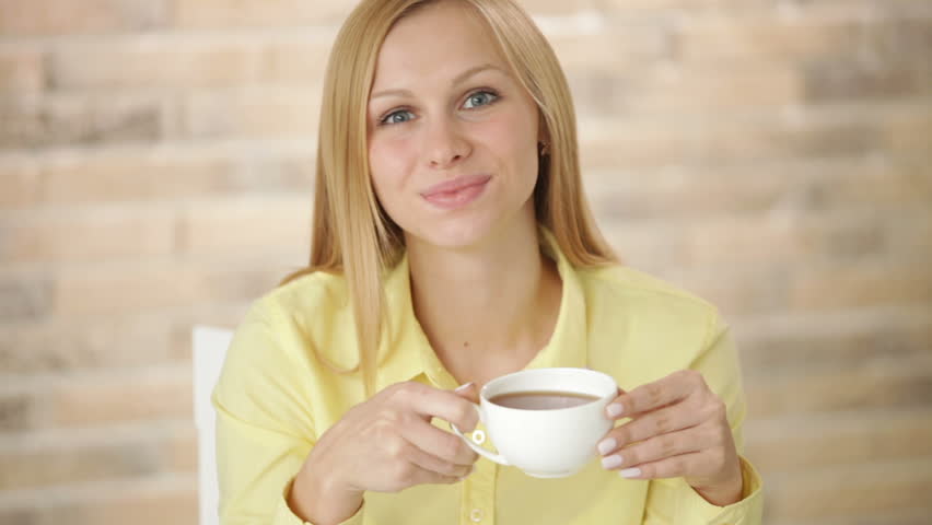 Attractive girl sitting at table with books and laptop drinking tea looking at