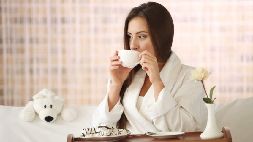 Charming girl relaxing on sofa drinking tea looking at camera and smiling.