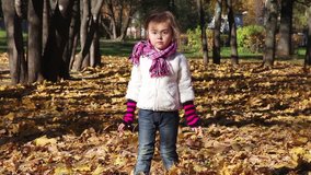 A four years old girl throws autumn leaves and laughs
