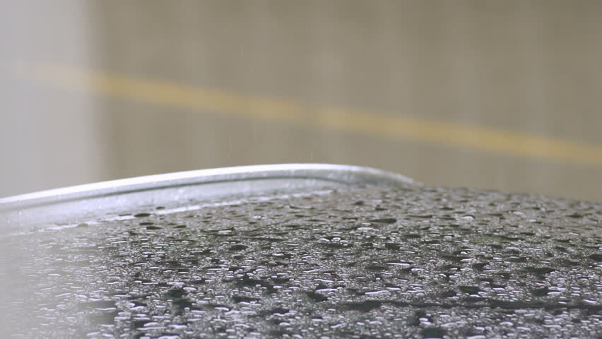 Slow Motion Shot Of Rain Drops Dripping On The Car Roof. A Pedestrian Passes By