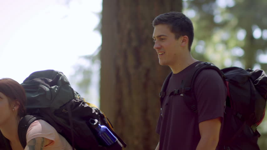 Fit and healthy young couple hikes through park and stops to take photo