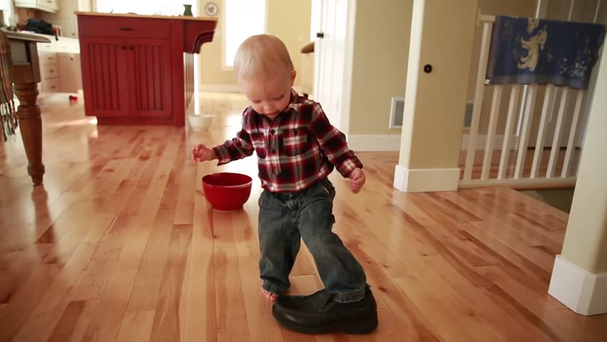 A little boy walking with his fathers shoes on