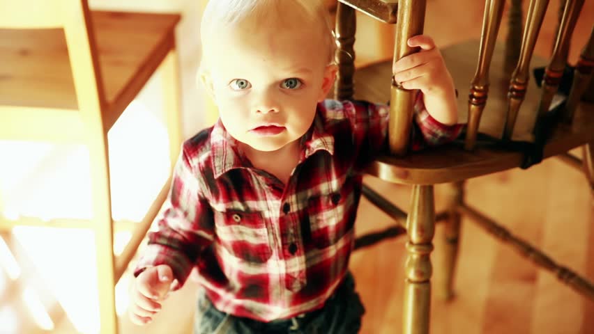 A cute little boy standing by his highchair in the kitchen waiting for food