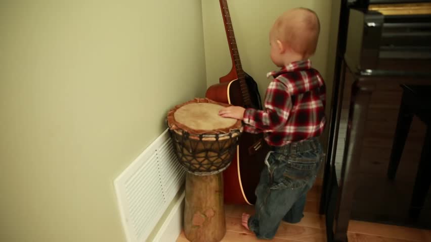 A little boy strumming the guitar and playing a drum
